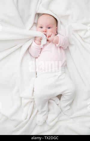 Ansicht von oben cute adorable Baby Mädchen mit weißem Körper im Schlafzimmer an der Kamera schaut. Neugeborene Kind ziehen Decke für den Mund im Bett Stockfoto