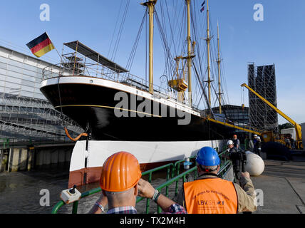 Wewelsfleth, Deutschland. 24. Juni, 2019. Das Segelschiff "Peking" liegt vor dem Trennen von einer Erweiterungsstation herunter, in der Werft, die Arbeitnehmer an der Pier stehen. Die traditionelle Sailor 'Peking' soll sich auf seine eigene Kiel wieder zu schwimmen nach einer längeren Liegezeit. Die Arbeiten sollen im Mai 2020 abgeschlossen sein. Die 'Peking' wird später seinen letzten Liegeplatz in der geplanten deutschen Hafen Museum im Hamburger Hafen haben. Credit: Carsten Rehder/dpa/Alamy leben Nachrichten Stockfoto