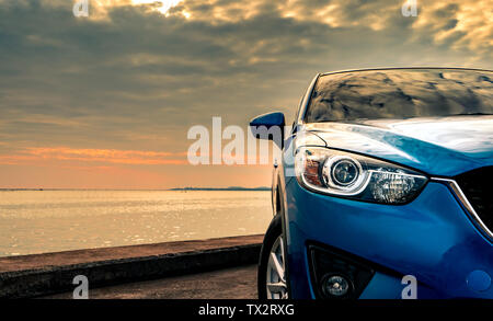 Blaue kompakte SUV-Auto mit Sport und modernes Design auf Beton durch das Meer geparkt bei Sonnenuntergang am Abend. Hybrid- und Elektroautos Technologie conc Stockfoto