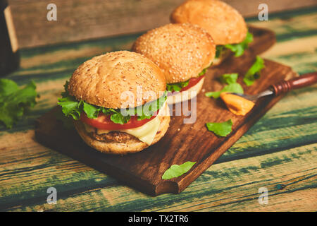 Handwerk Beef Burger auf Holztisch auf schwarzem Hintergrund isoliert. Street Food, Fast Food. Hausgemachte saftige Burger mit Käse und auf dem Holztisch. Stockfoto