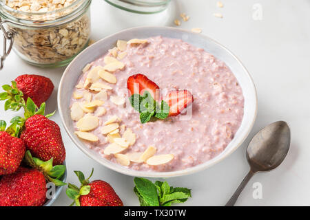Gesundes Frühstück. Über Nacht Hafer mit frischen Erdbeeren, Mandeln und Minze in eine Schüssel geben und mit einem Löffel auf weißem Marmortisch. Nach oben Schließen Stockfoto