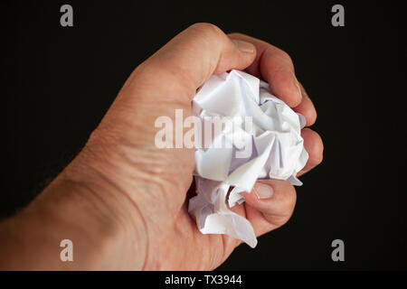 Hand Curling ein Stück Papier auf schwarzem Hintergrund. Schließen Sie herauf Bild Stockfoto
