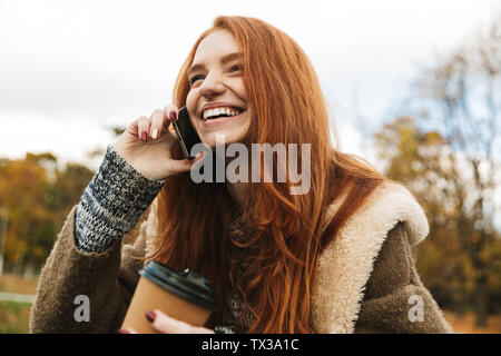 Schöne rothaarige Mädchen sitzen auf einer Bank, mit Handy Stockfoto