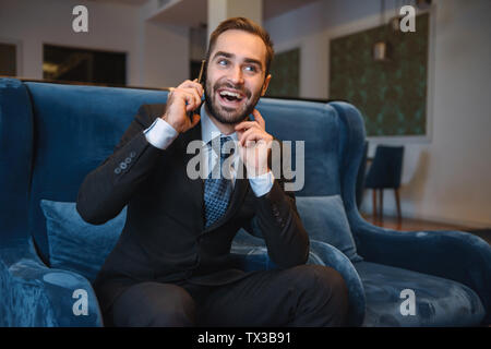 Hübscher junger Unternehmer tragen Anzug in der Lobby sitzen, mit Handy Stockfoto