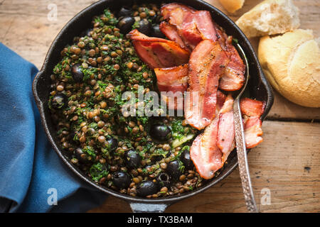 Braune Linsen mit Spinat, schwarze Oliven und gebratener Speck Stockfoto