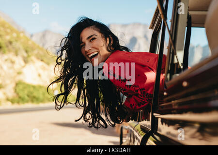 Hübsche junge Frau auf der Suche aus dem Auto und Lachen. Frau, eine tolle Zeit während von einem Auto auf einer Straße Reise reisen. Stockfoto