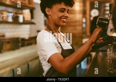 Afrikanische Frauen barista über eine Kaffeemaschine eine schöne Tasse Kaffee zu machen. Cafe Arbeiter Vorbereitung einen Kaffee. Stockfoto