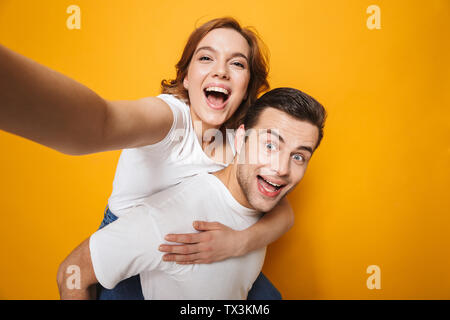 Porträt einer fröhlichen jungen Paar auf gelben Hintergrund isoliert, piggyback Ride, wobei selfie Stockfoto