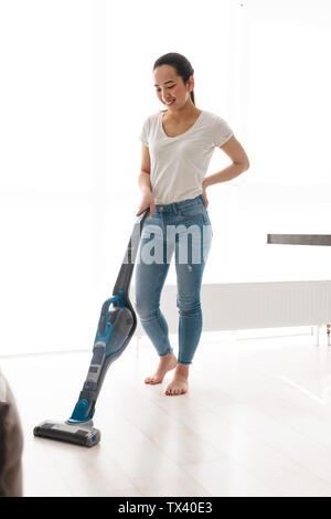 Portrait von fröhlichen asiatische Frau 20 s Hausarbeit tun mit Staubsauger im hellen Zimmer zu Hause Stockfoto