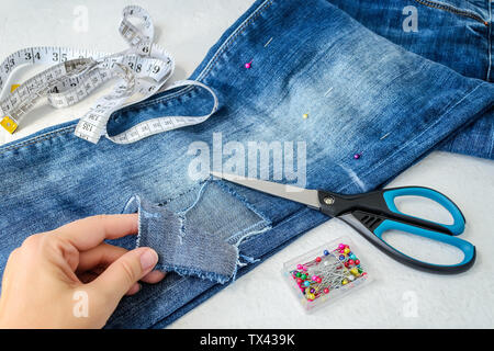 Frau Hand zeigt ein großes Loch auf Pant Bein einer blauen Jeans in der Hälfte gefaltet. Jeans sind zum Ausschneiden für Denim Shorts vorbereitet. Mit Schere, p Stockfoto