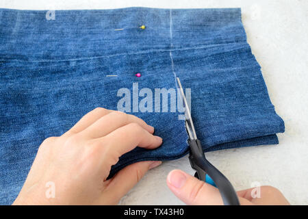 Woman hand holding a scissors and cutting blue denim shorts to make them shorter. Making jeans shorts. On a white background. Stockfoto