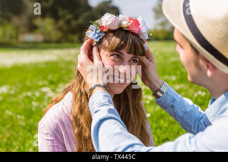 Junger Mann Blumen setzen auf auf den Kopf seiner Freundin Stockfoto