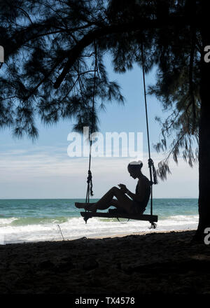 Thailand, Krabi, Lao liang Insel, Frau auf Baum schwingen am Strand Stockfoto