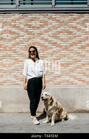 Lachende Frau, die neben ihrem Labrador Retriever vor gemusterte Mauer Stockfoto