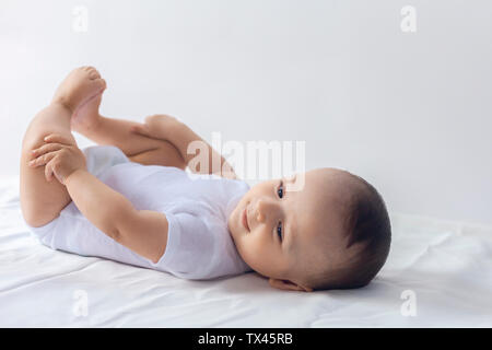 6-monatiges Baby Spaß in weißer Bettwäsche. Cute Baby liegend auf dem Bett. Familie, neue Leben, Kindheit Konzeption. Stockfoto