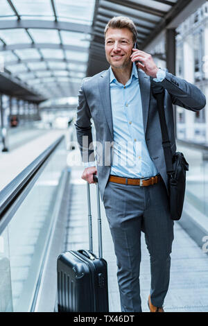 Lächelnd Geschäftsmann mit Gepäck und Handy auf fahrsteig Stockfoto