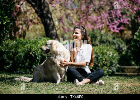 Gerne Frau sitzt auf der Wiese im Stadtpark mit ihrem Labrador Retriever Sonnenlicht genießen. Stockfoto