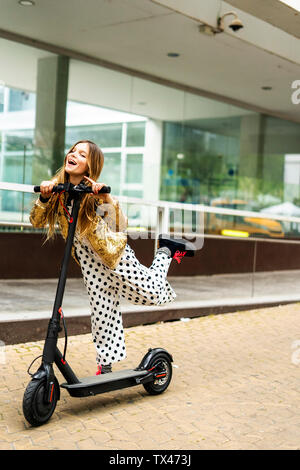 Portrait von lachenden Mädchen mit E-Scooter tragen goldene Pailletten Jackett und Polka Dot jumpsuit Stockfoto