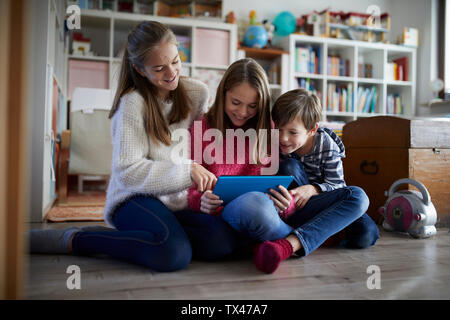 Geschwister spielen zu Hause mit Ihren digitalen Tabletten, sitzend auf dem Boden Stockfoto