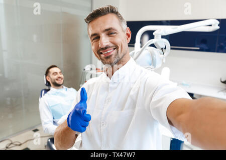 Bild von einem gutaussehenden jungen Mann gerne Arzt in medizinischen Zahnarzt Zentrum zeigt eine selfie durch die Kamera. Stockfoto