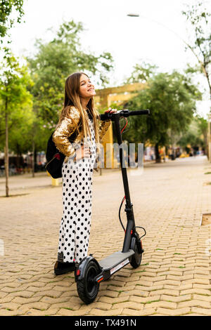 Glückliches Mädchen mit E-Scooter tragen goldene Pailletten Jackett und Polka Dot jumpsuit Stockfoto