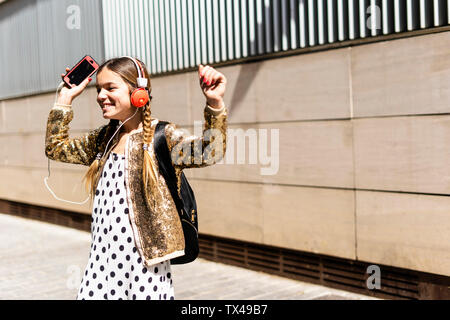 Lächelnde Mädchen mit Kopfhörern und Smartphone tanzen auf der Straße Stockfoto