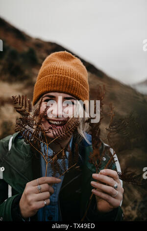 Großbritannien, Schottland, Highlands, Porträt der glückliche junge Frau mit Farn Stockfoto