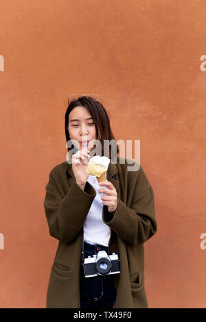 Junge Frau essen ein Eis in einem orange Wand Stockfoto