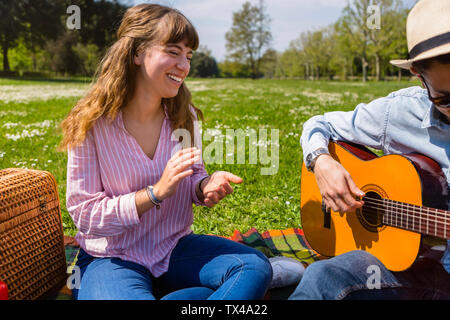 Junger Mann an der Gitarre für seine Freundin in einem Park Stockfoto