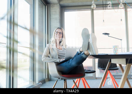 Entspannt Geschäftsfrau mit Laptop im Büro mit Fuß oben Stockfoto