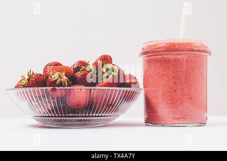 Strawberry Smoothie in Glas und einer Schale mit frischen Beeren auf weißem Hintergrund, close-up. Stockfoto