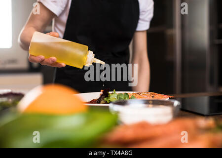 In der Nähe von Frau Kochen in der Küche gießen Olivenöl auf einem Teller Stockfoto