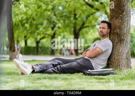 Mann gegen einen Baum im Park mit einem nap Schiefen Stockfoto