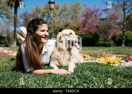 Glückliche Frau liegend auf der Wiese im Stadtpark mit ihrem Labrador Retriever genießen Sonnenlicht Stockfoto