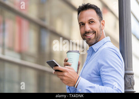 Lächelnd Geschäftsmann mit mit Takeaway Kaffee und Handy in der Stadt Stockfoto