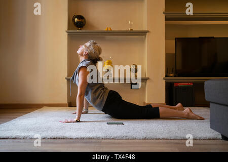 Reife Frau Yoga Übung im Wohnzimmer Stockfoto