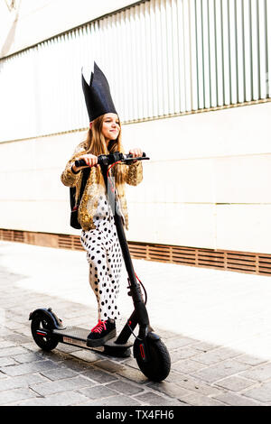 Portrait von lächelnden Mädchen mit E-Scooter mit schwarzen Krone, goldenen Pailletten Jackett und Polka Dot jumpsuit Stockfoto