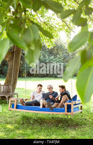 Die Männer der Familie auf einer Schaukel sitzend Bett ing den Garten, Reden, mit digitalen Tablet Stockfoto