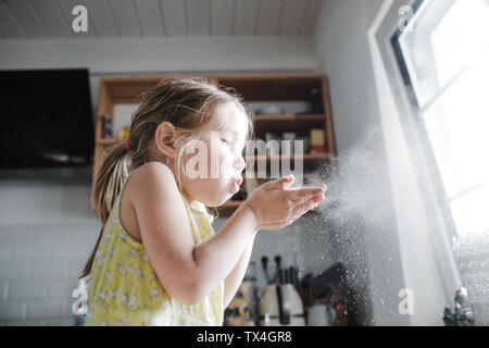 Kleine Mädchen bläst Mehl in die Luft in der Küche Stockfoto