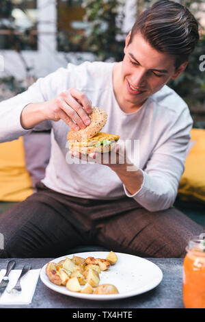 Junger Mann saß auf der Couch in einem Restaurant in eine vegane Burger zum Mittagessen Stockfoto