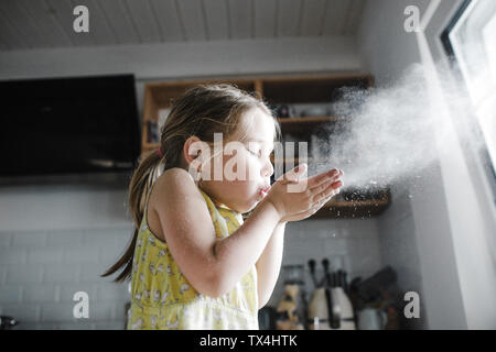 Kleine Mädchen bläst Mehl in die Luft in der Küche Stockfoto