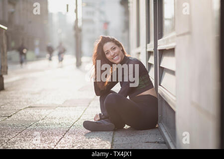 Portrait von glücklich sportliche junge Frau auf dem Boden sitzend in der Stadt Stockfoto