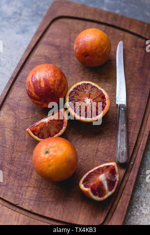 Ganze und aufgeschnittene Blutorangen und einem Küchenmesser auf Holzbrett Stockfoto