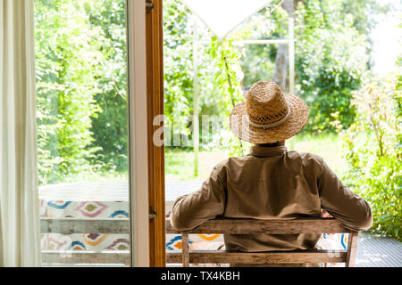 Rückansicht des älteren Mann mit Strohhut auf der Terrasse seinen Garten genießen. Stockfoto