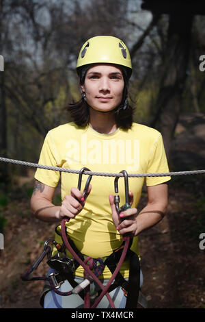 Junge Frau tragen gelbe T-Shirt und Helm in einem Hochseilgarten Stockfoto