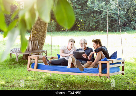 Die Männer der Familie auf einer Schaukel sitzend Bett ing den Garten, Reden, mit digitalen Tablet Stockfoto