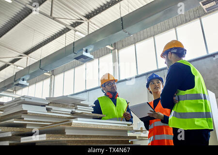 Zwei Männer und eine Frau in Warnwesten diskutieren in der Factory Stockfoto