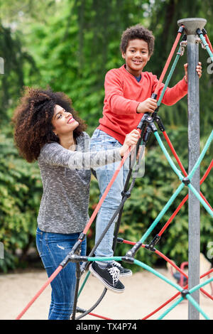 Mutter und Sohn spielen auf dem Spielplatz im Park, klettern in einem Jungle Gym Stockfoto