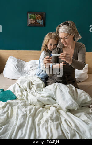 Mutter, die Temperatur der kranken Tochter im Bett liegend Stockfoto