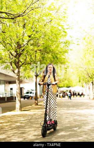 Portrait von glücklichen Mädchen auf E-Scooter tragen goldene Pailletten Jackett und Polka Dot jumpsuit Stockfoto